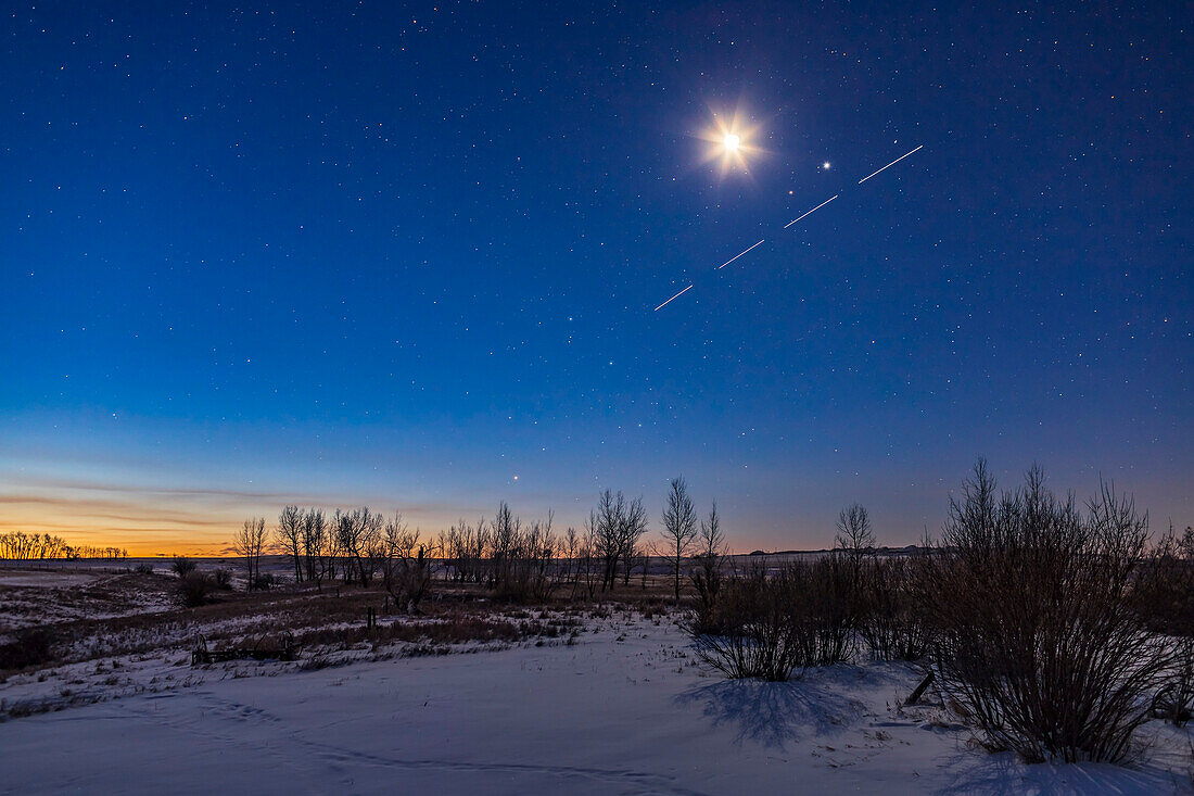 Ein belebter Morgenhimmel, mit der abnehmenden Mondsichel, die über dem Paar von Mars (links) und Jupiter (rechts) leuchtet, und der Raumstation, die ebenfalls in vier Belichtungen vorbeizieht. Der Mond und die Planeten stehen in Waage. Links von der Mitte gehen Antares und die Sterne des Skorpions gerade in der Morgendämmerung auf.