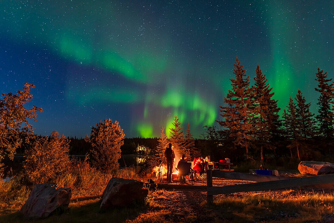 An einem schönen September-Samstagabend genießt man ein Lagerfeuer unter den heller werdenden Nordlichtern am Madeline Lake auf dem Ingraham Trail in der Nähe von Yellowknife. Der Blick geht nach Nordosten zu Perseus mit den aufgehenden Plejaden.