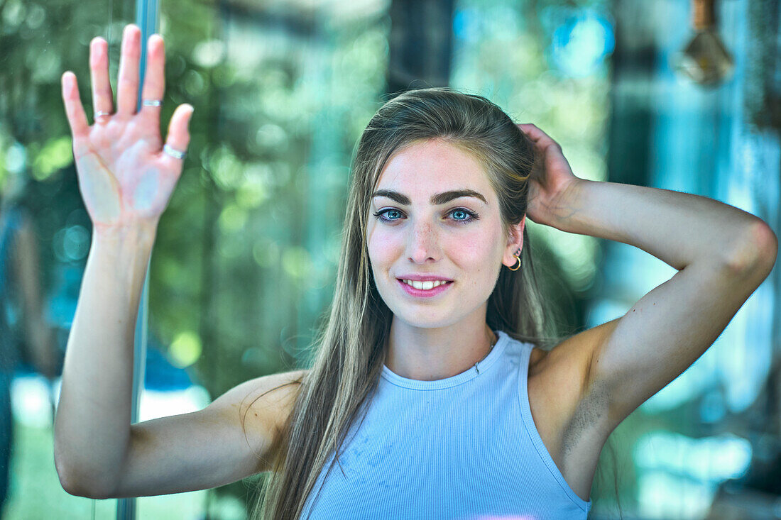 Portrait of a young beautiful caucasian woman in her 20´s with long hair and blue eyes leaning with her hands on a glass. Lifestyle concept.