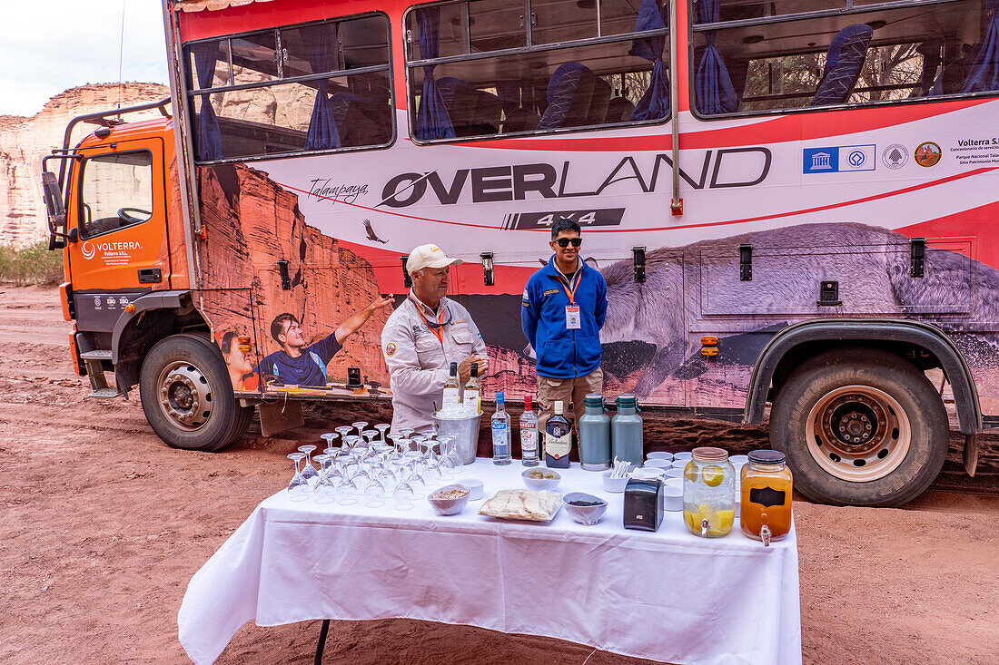 Führer verteilen Erfrischungen auf einer Tour im Talampaya-Nationalpark, Provinz La Rioja, Argentinien. Dahinter steht ein Reisebus mit Allradantrieb.