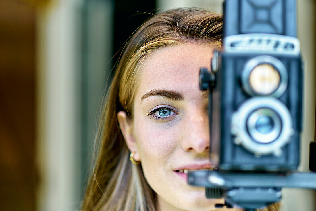 Porträt einer jungen schönen kaukasischen Frau in den 20ern mit blauen Augen beim Fotografieren mit einer alten Vintage-Kamera auf einem Stativ im Freien. Lifestyle-Konzept.