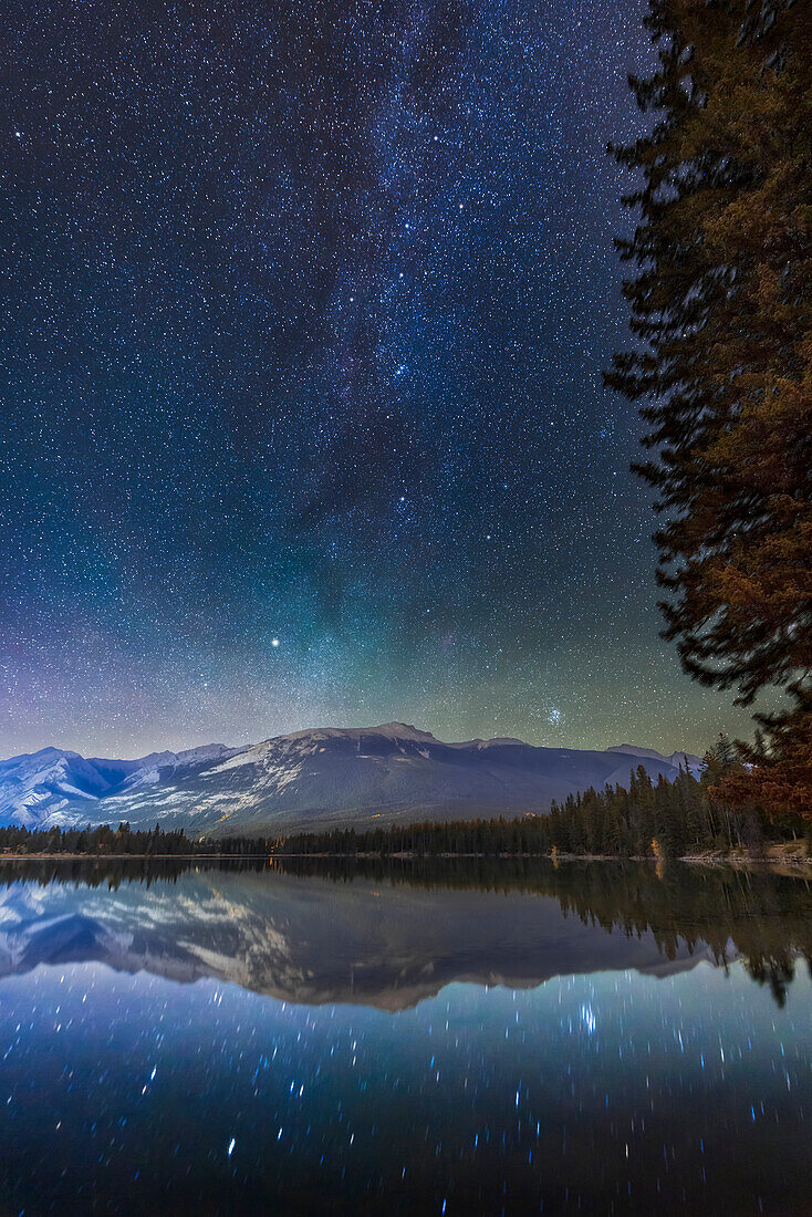 The autumn constellations of Perseus and Cassiopeia above, with bright Capella in Auriga and the Pleiades star cluster in Taurus, at bottom, rising in the northeast over Lake Edith in Jasper National Park, on a clear autumn night. The Double Cluster is at centre, above the larger group of stars around Mirfak called the Perseus Association.