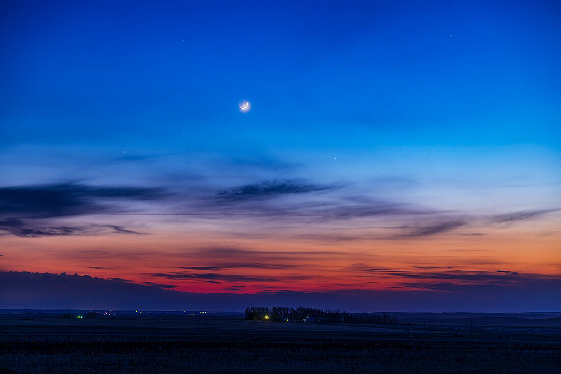 The two-day-old waxing crescent Moon with Earthshine, above Mercury at right, then 4 days past its greatest elongation from the Sun, in the evening sky of May 2, 2022. The star Aldebaran is at left, and below Mercury to the right is the Pleiades, just visible in the twilight and thin clouds.