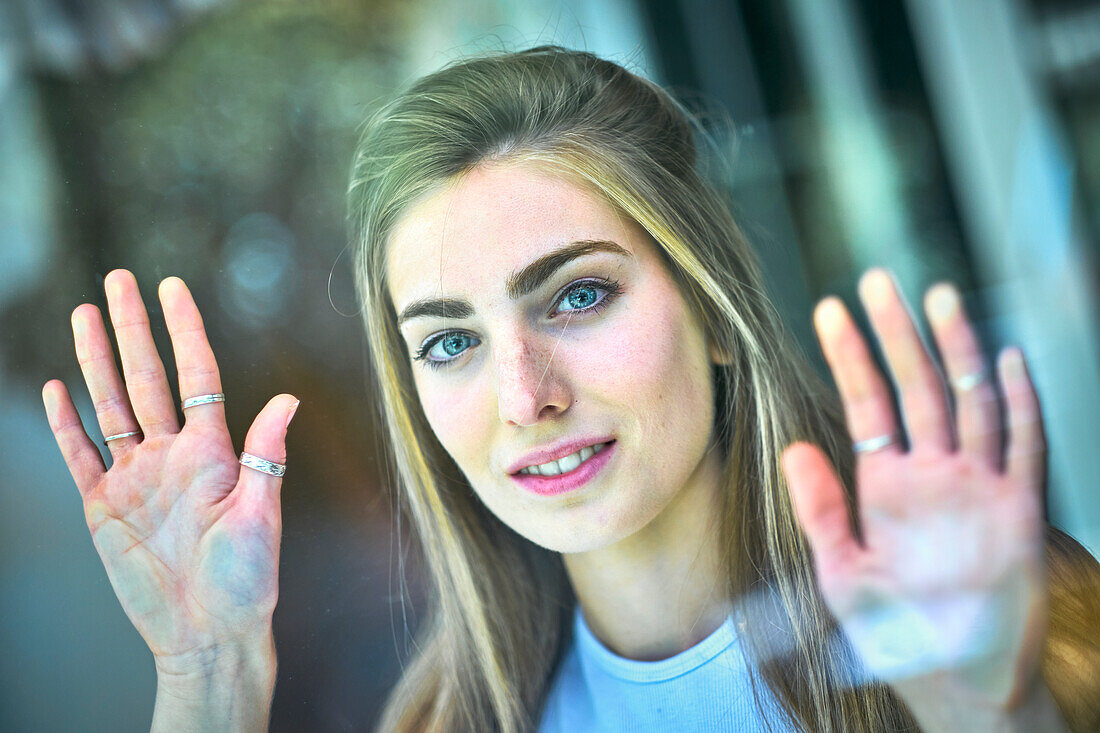 Portrait of a young beautiful caucasian woman in her 20´s with long hair and blue eyes leaning with her hands on a glass. Lifestyle concept.