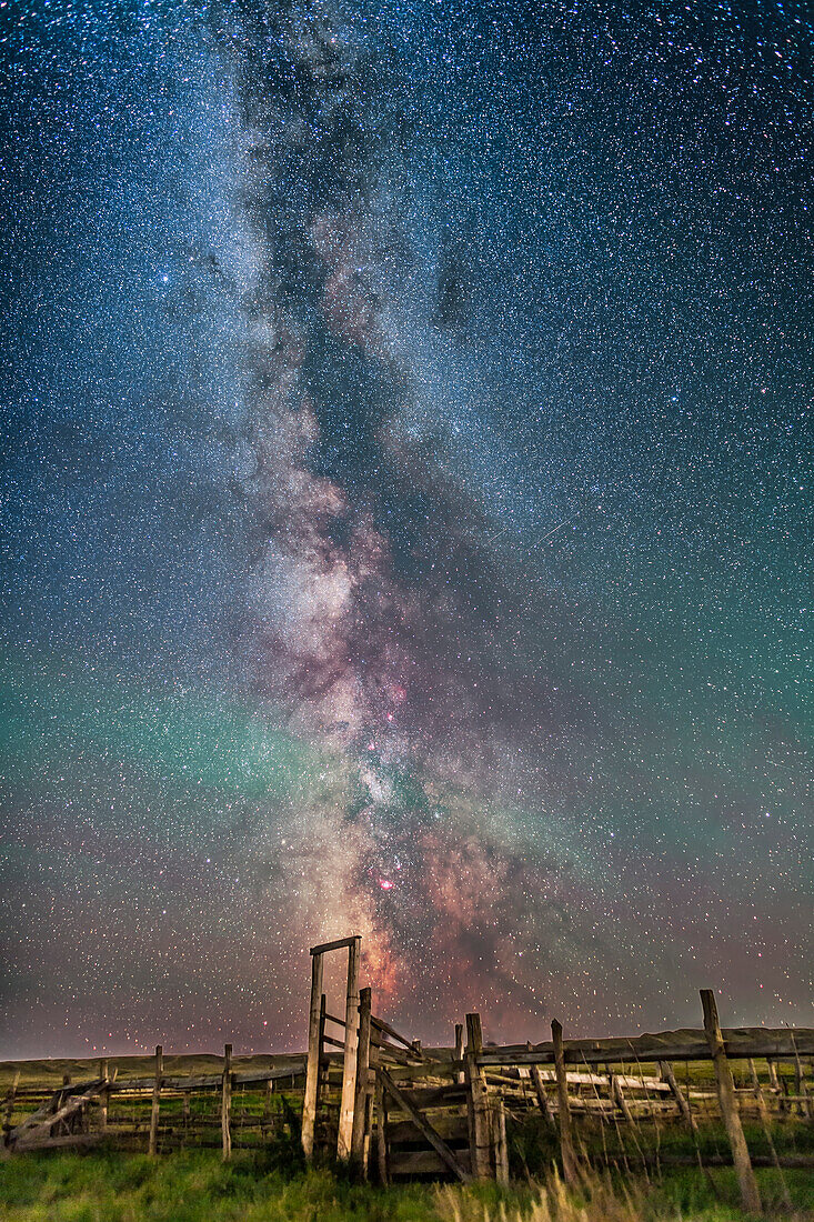 Die Milchstraße über dem alten Korral auf dem Gelände der 76 Ranch im Frenchman Valley im Grasslands National Park, Saskatchewan. Ich habe dies am 26. August in einer perfekten Nacht aufgenommen, in der die Aurora zu leuchten begann, aber noch nicht sehr hell war, so dass der Himmel dunkel war. Der Vordergrund wird vom Sternenlicht, von der im Norden aufleuchtenden Aurora und von den gelegentlichen Scheinwerferlichtern der Naturforscher im Tal beleuchtet, die nach nachtaktiven Frettchen Ausschau halten. Die grünen Streifen am Himmel stammen vom natürlichen Glühen der Luft.