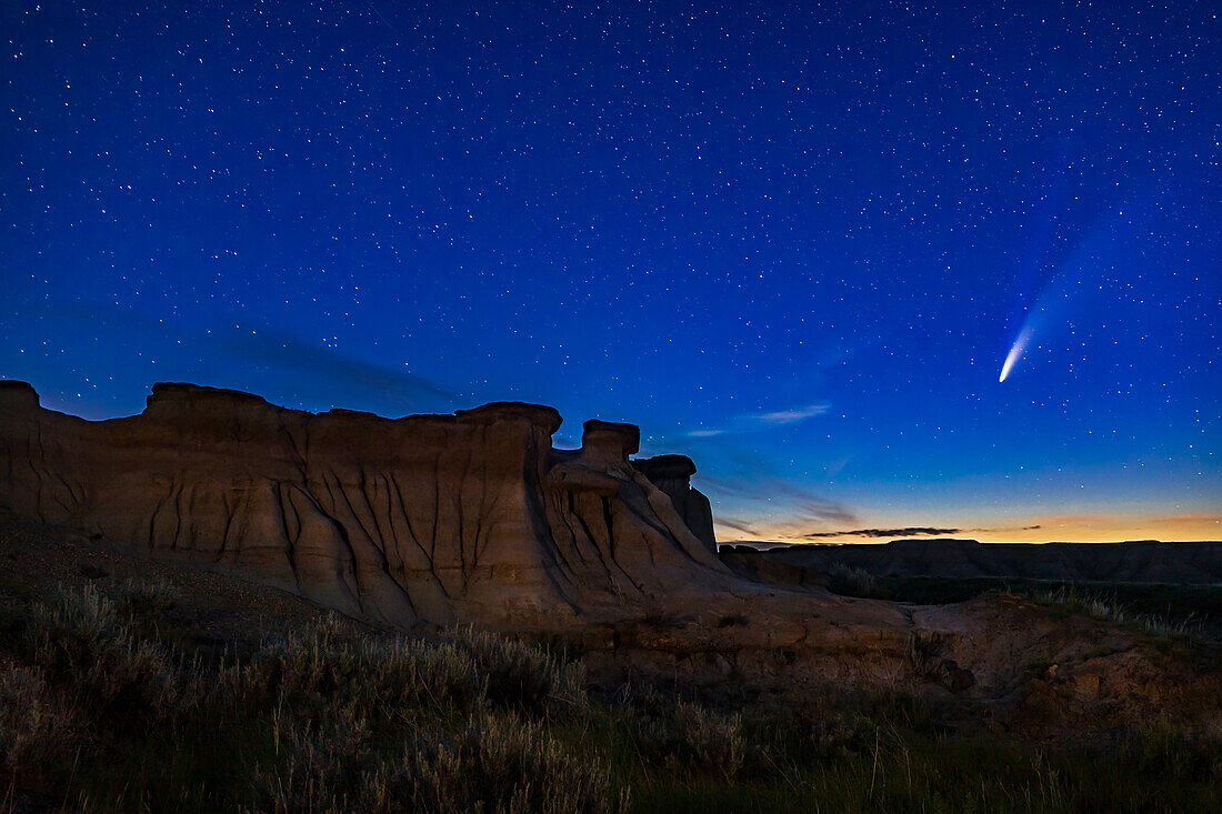 Komet NEOWISE (C/2020 F3) über einigen der erodierten Hoodoo-Formationen im Dinosaur Provincial Park, Alberta, 14-15 Juli 2020. Die Dämmerung färbt den Himmel. In diesem Fall ist der Vordergrund mit einem warmen LED-Licht leicht beleuchtet. Diese Aufnahme stammt von der Website Trail of the Fossil Hunters.