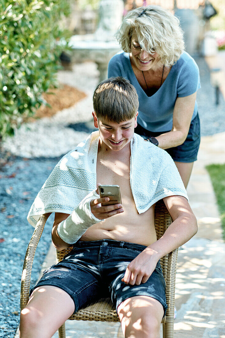 Porträt einer Mutter, die einem jungen kaukasischen Jungen draußen im Garten die Haare schneidet. Lifestyle-Konzept.