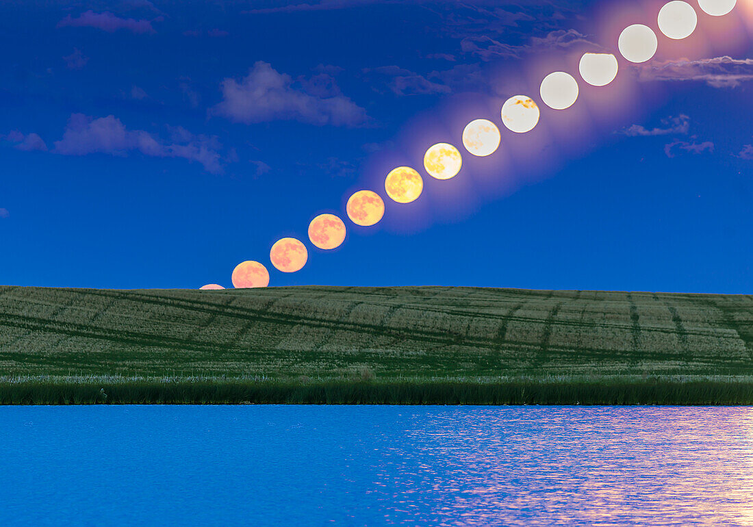 The rising Full Moon of June, dubbed the “Strawberry Moon” in the media, as seen rising over a prairie pond in southern Alberta, on June 9, 2017. At right, the glitter path from the Moon also combines on the water.