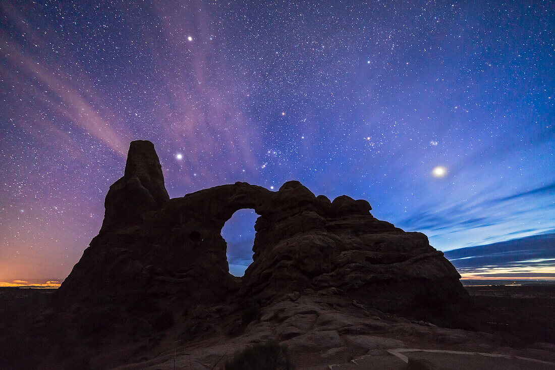 Orion und der Winterhimmel mit der Venus, die in der westlichen Dämmerung untergeht, über dem Turret Arch im Arches National Park, Utah, am 6. April 2015. Die Venus ist das helle Objekt rechts unter den Pleaiden. Sirius ist der helle Stern links, Procyon der helle Stern oben links.