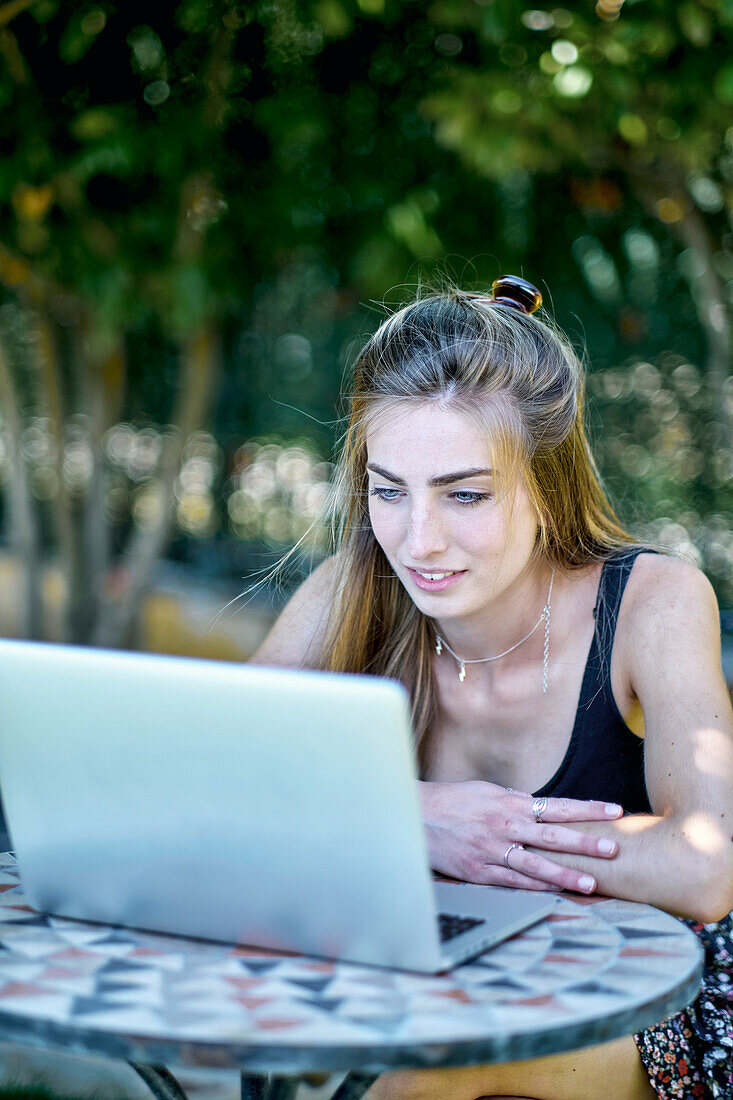 Porträt einer jungen kaukasischen Frau, die im Freien in einem Garten mit einem Laptop posiert und nach Informationen im Internet sucht. Lebensstil-Konzept.
