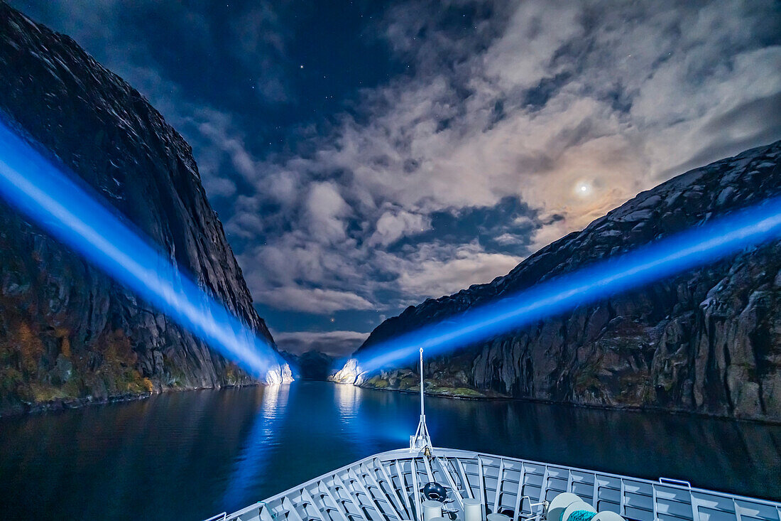 Exiting the narrow Trollfjord by searchlight and under moonlight, on the northbound voyage of the Hurtigruten ferry ship the ms Trollfjord, on October 15, 2019. Capella is at top; Betelgeuse and Orion are rising at centre at the mouth of the fjord; Aldebaran is partly in cloud left of the Moon.