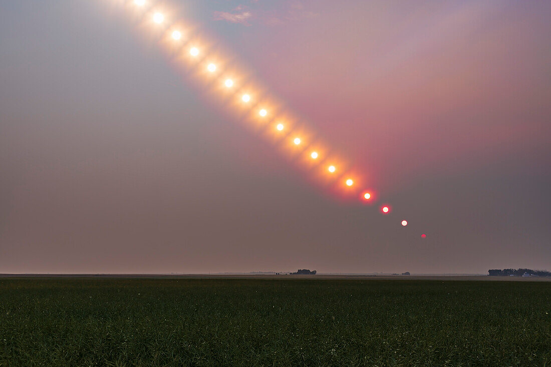 Die Sonne geht am 17. August 2018 in einer Wolke aus Waldbrandrauch über Alberta unter, der von Bränden in B.C. und anderswo stammt. Dies zeigt die Verdunkelung und Rötung der Sonne bei ihrem Untergang, wobei sie aus dem Bild verschwindet, lange bevor sie den Horizont erreicht.