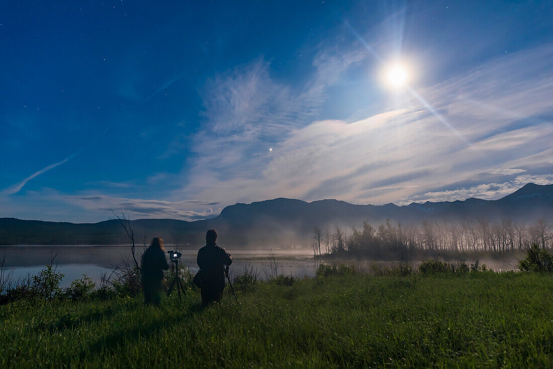 Fotografen bei einem meiner Nachtaufnahmen-Workshops, 14. Juni 2019, am Maskinonge Pond im Waterton Lakes National Park, Alberta, Kanada, mit dem Mond und Jupiter am Himmel.