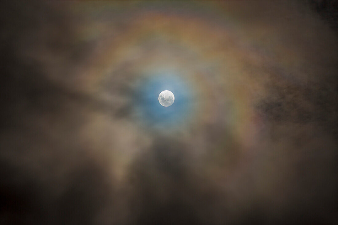 Der Beinahe-Vollmond vom 10. April 2017 von Australien aus gesehen, eingebettet in sich schnell bewegende niedrige Wolken, die den farbenfrohen Koronaeffekt um den Mond durch die Beugung von Wassertröpfchen hinzufügen.