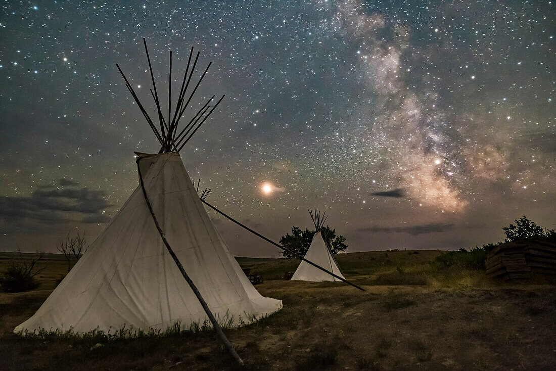 Mars und die Milchstraße über den Tipis im Two Trees Gebiet im Grasslands National Park, Saskatchewan am 6. August 2018. Einige leichte Wolken fügten den Planeten und Sternen Dunst und Glühen hinzu. Die Beleuchtung erfolgt durch Sternenlicht. Hier wurde keine Lichtmalerei verwendet.