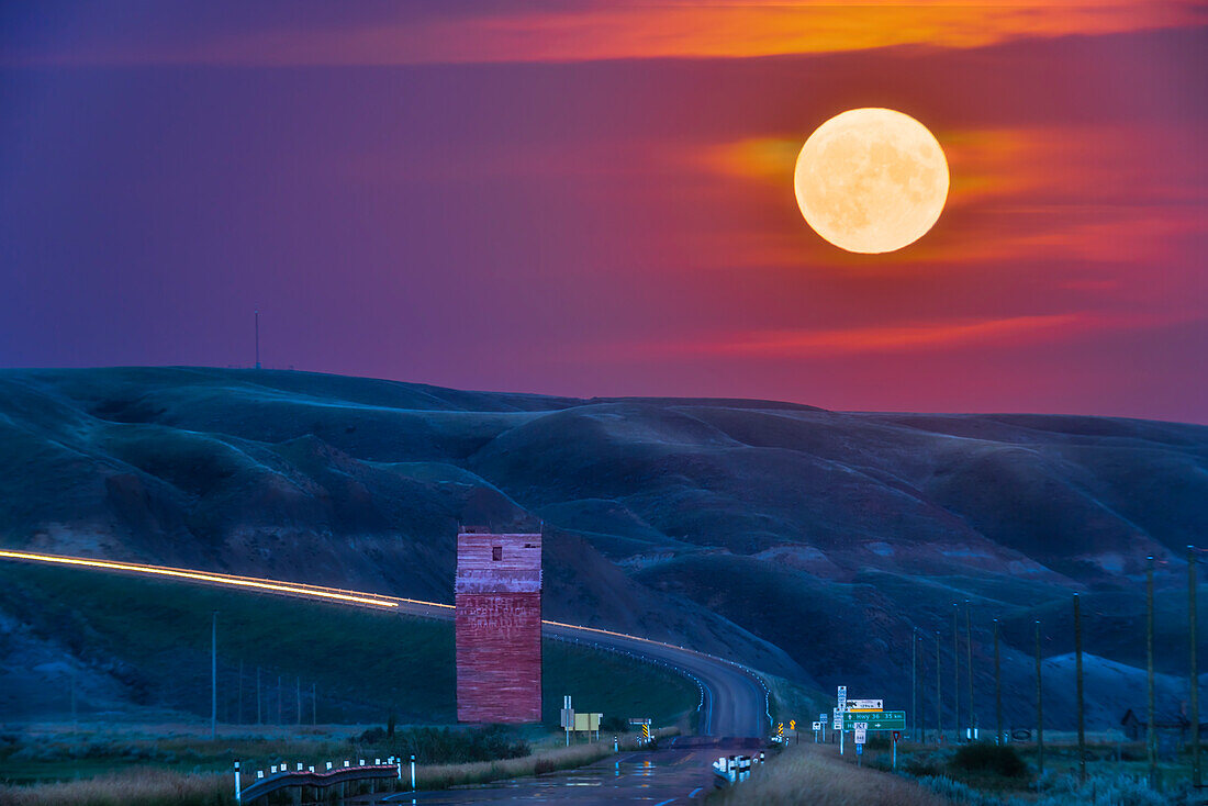 Der Vollmondaufgang vom 11. August 2022 über dem alten Getreidesilo am Highway 10 bei Dorothy, Alberta, in den Badlands des Red Deer River Valley. In den populären Medien wurde er als "Supermond" und "Störmond" bezeichnet. Er ging zufällig an einem Ort auf, an dem er genau auf dem nach Südosten führenden Highway im Tal stand.