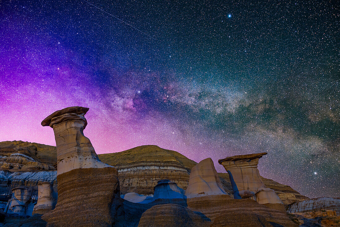 The summer Milky Way in Cygnus, with the Summer Triangle stars rising over the Hoodoos formations on Highway 10 near Drumheller, Alberta. A low-level aurora display tints the sky magenta and blue at left, making for an unusually colourful sky. The bright stars are: Vega is at top, Deneb at centre and Altair at bottom right.
