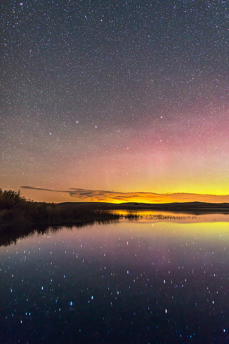 Der Große Wagen spiegelt sich im stillen Wasser des Sees im Police Outpost Provincial Park im Süden von Alberta am 26. September 2016, mit einem Polarlicht im Norden rechts. Nur im Herbst kann man den Großen Wagen, der sich im Wasser spiegelt, am Abendhimmel fotografieren, da er dann tief am nördlichen Horizont steht. Dies ist von 49° nördlicher Breite aus aufgenommen, wo die Wasseramsel zirkumpolar ist. In Großbritannien wird er auch "Plough" genannt.