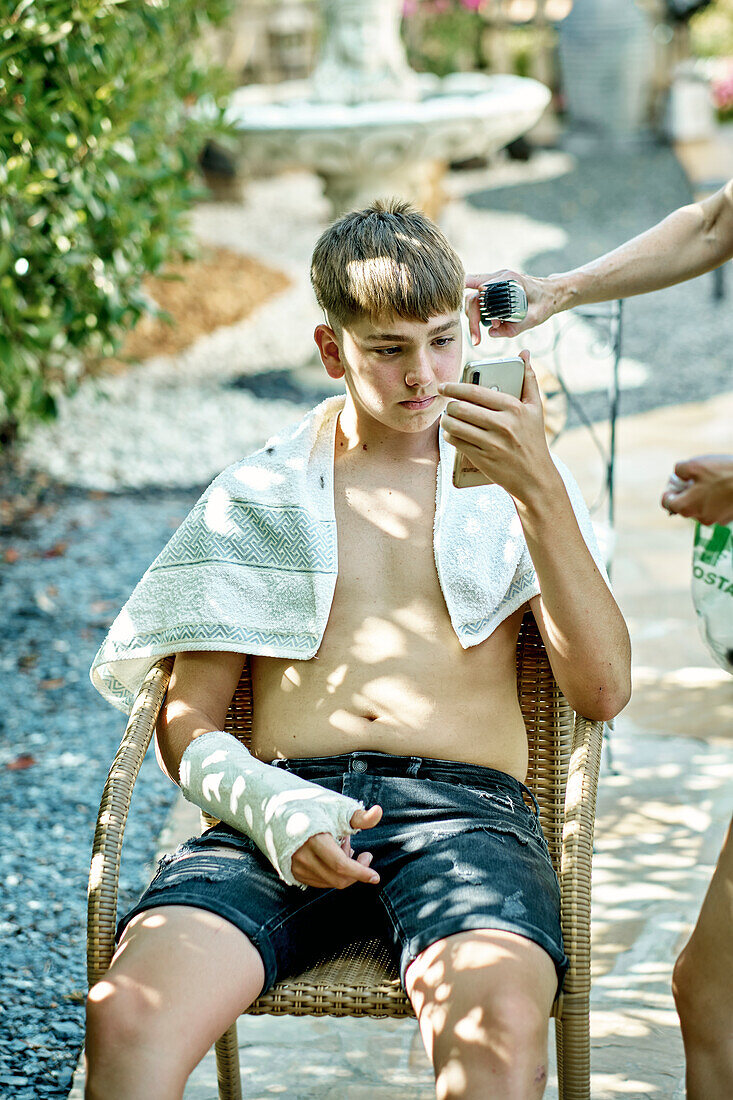 Porträt einer Mutter, die einem kleinen kaukasischen Jungen draußen im Garten die Haare schneidet. Lebensstil-Konzept.