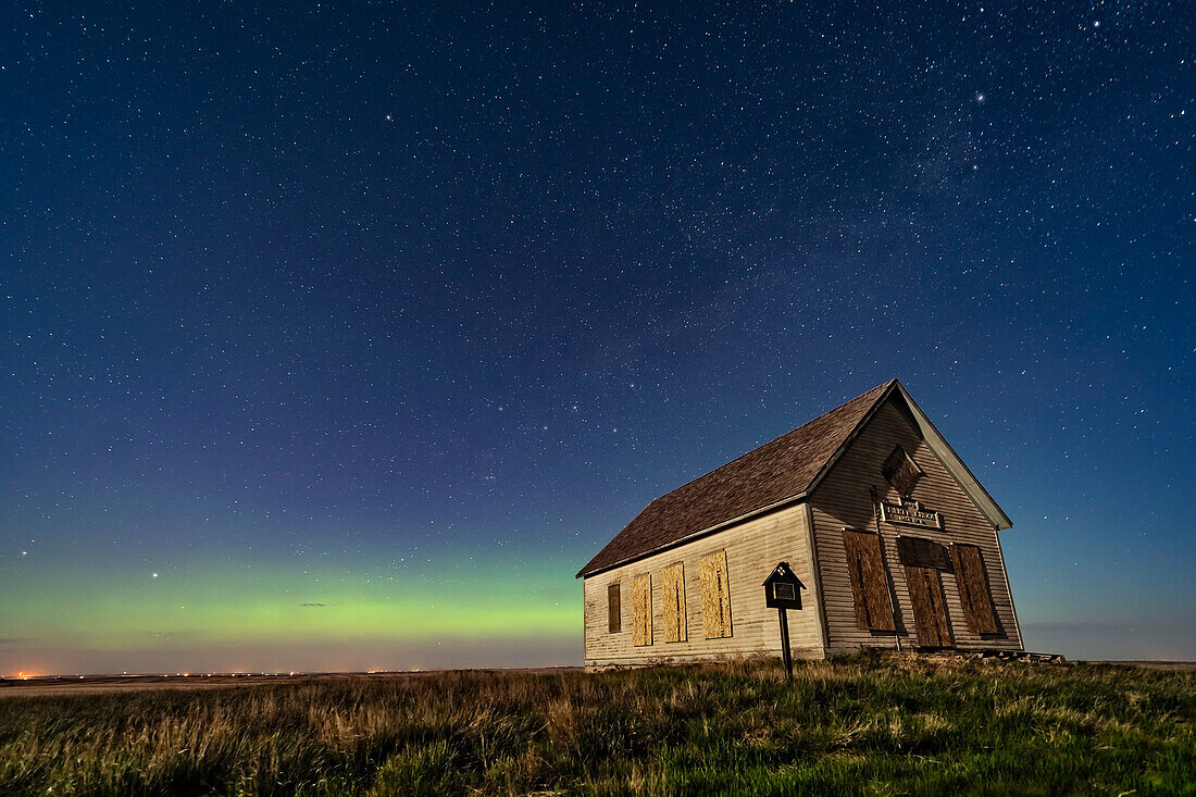 Das Liberty Schoolhouse von 1910, eine Einraumschule der Pioniere, in der Prärie von Alberta in der Nähe von Majorville, im Mondlicht mit einem Polarlicht im Norden. Polaris ist oben links. Kassiopeia befindet sich oberhalb der Schule. Der 8-tägige zunehmende Mond sorgt für die Beleuchtung.
