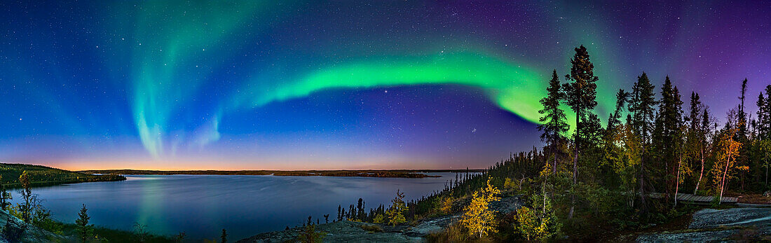 The arc of Northern Lights starting a show in the deep twilight over Prelude Lake on the Ingraham Trail near Yellowknife, NWT. This was September 9, 2019. Light from the waxing gibbous Moon behind the camera also illumimates the scene. The autumn colours make for a good contrast with the sky colours. This was from the lookout point above the lake and main parking area and boat launch.