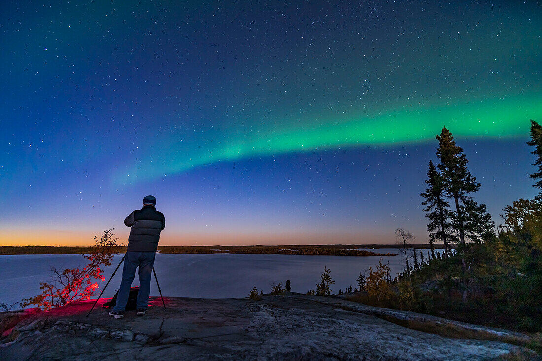 Der Fotograf Stephen Bedingfield bereitet sich auf die Aufnahme des Nordlichts am Prelude Lake in der Nähe von Yellowknife, NWT, am 9. September 2019 vor. Sogar am Dämmerungshimmel beginnt ein Polarlichtbogen zu erscheinen.