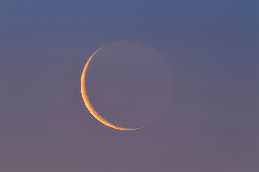 The thin waning 26-day-old Moon low in the dawn sky and reddened from the low altitude and twilight colours, but still showing some Earthshine on the dark side of the Moon.