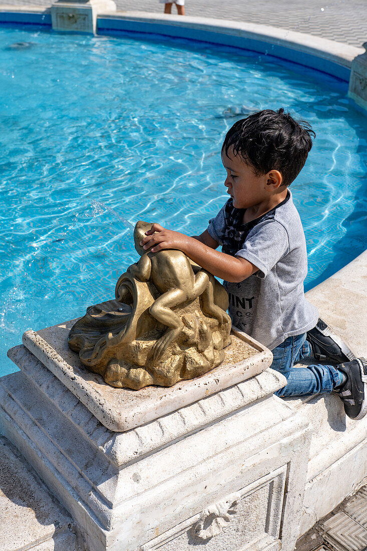 Ein kleiner Junge spielt im Springbrunnen auf dem Plaza 25 de Mayo oder Hauptplatz in San Juan, Argentinien.
