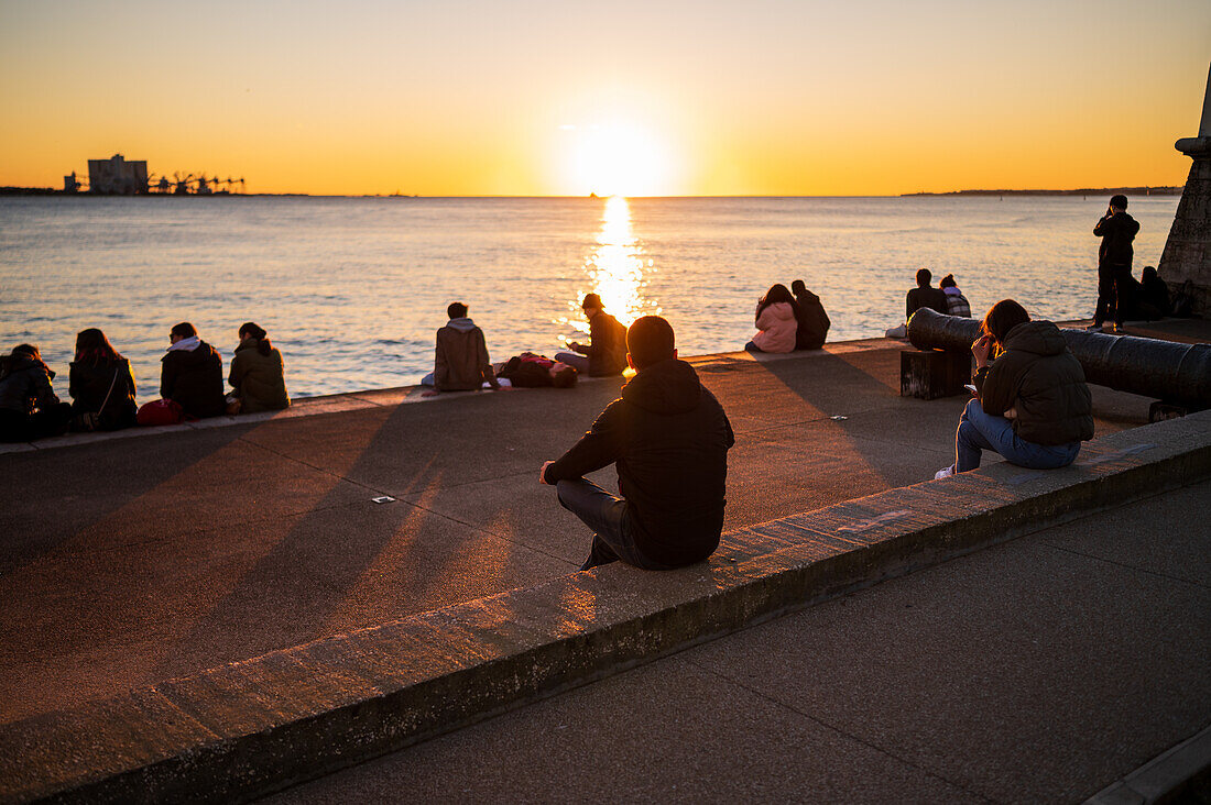 People enjoy a beautiful sunset from Belem Tower or Tower of St Vincent on the bank of the Tagus River, Lisbon, Portugal