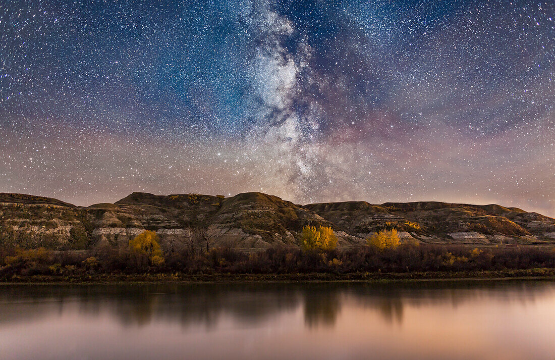 The Milky Way in Sagittarius (toward the galactic centre) going down behind the badland hills along the Red Deer River. I shot this near East Coulee on Highway 10 in Alberta, on an autumn night. Some clouds were drifting through over the exposure times. Passing car headlights helped light the trees on the opposite bank.