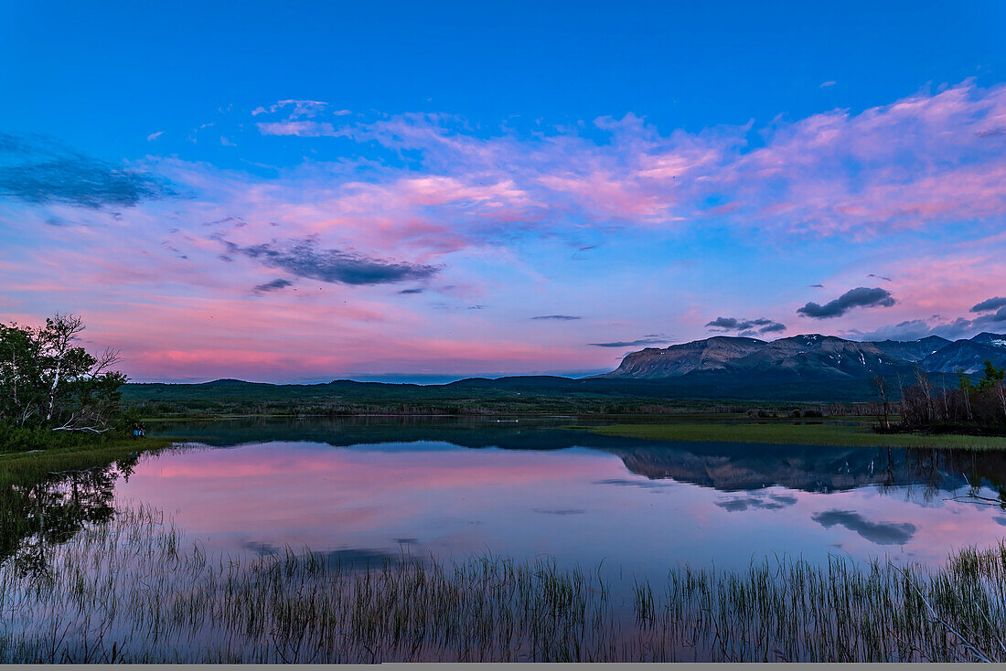 Two photographers and participants at my June 17, 2018 Night Photography Workshop in Waterton Lakes National Park, at Maskinonge, in the evening twilight, with the twilight colours over the lake. Two swans are in the distance. This was a magical evening.