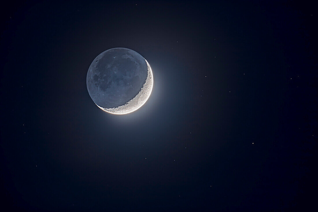 Erdschein beleuchtet die dunkle Seite des Mondes bei der zunehmenden Mondsichel am 27. Februar 2020. Sterne umgeben den Mond am tiefen Dämmerungshimmel. Der hellste Stern ist Nu Piscium mit 4,4 Magnituden.
