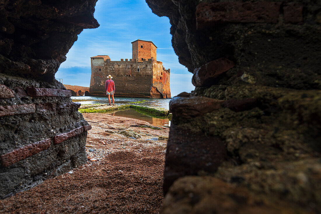 Blick von unten auf einen Mann vor der Burg von Torre Astura durch ein Loch in der Mauer gesehen, Provinz Rom, Tyrrhenisches Meer, Latium (Lazio), Italien, Europa