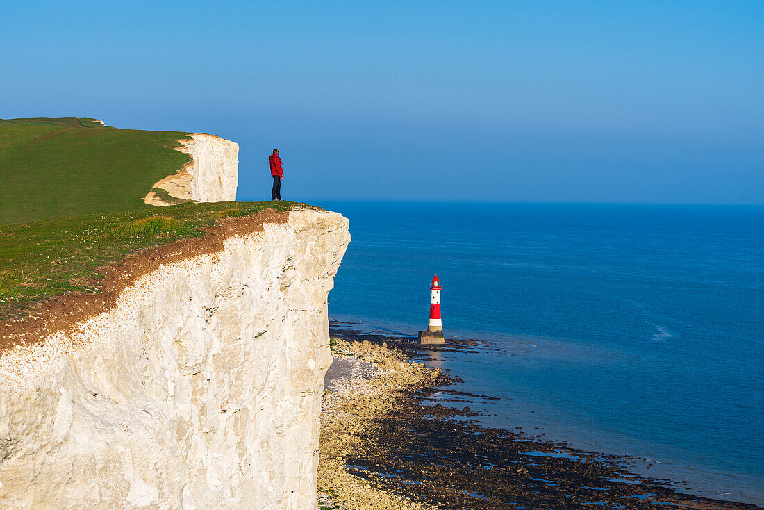 Tourist stands on top of the cliff overlooking Beachy Head lighthouse, Seven Sisters chalk cliffs, South Downs National Park, East Sussex, England, United Kingdom, Europe