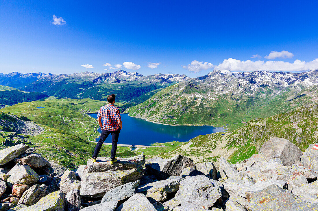 One man looking at the alpine lake of Montespluga standing on rocks, Madesimo, Valle Spluga, Valtellina, Lombardy, Italy, Europe