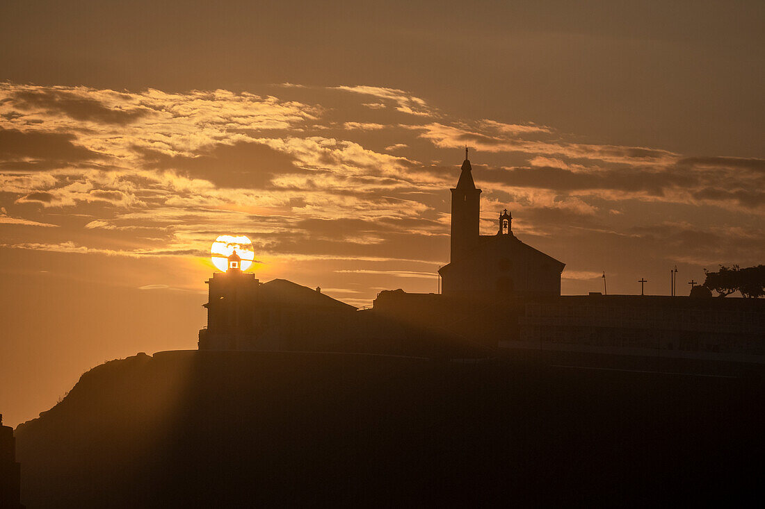 Sun aligned with the silhouette of the lighthouse and church of Luarca, Asturias, Spain, Europe