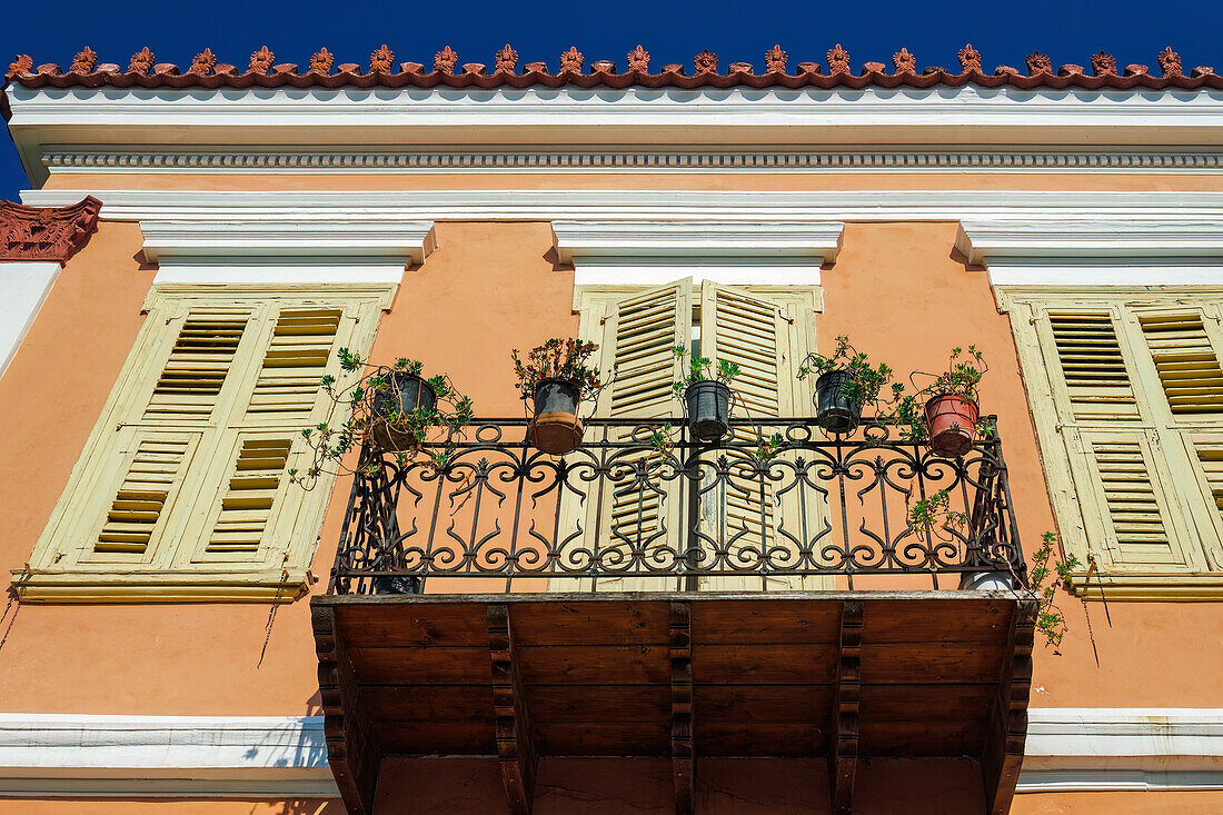 Tiefblick auf ein traditionelles Haus mit geschlossenen Holzläden und einem Balkon mit Pflanzentöpfen vor blauem Himmel in Nafplion, Peloponnes, Griechenland, Europa