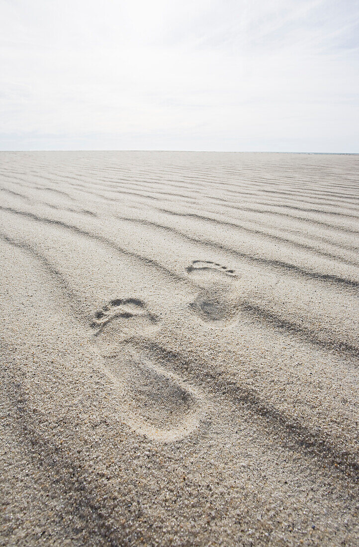 Fußabdrücke auf gewelltem Sand am Strand