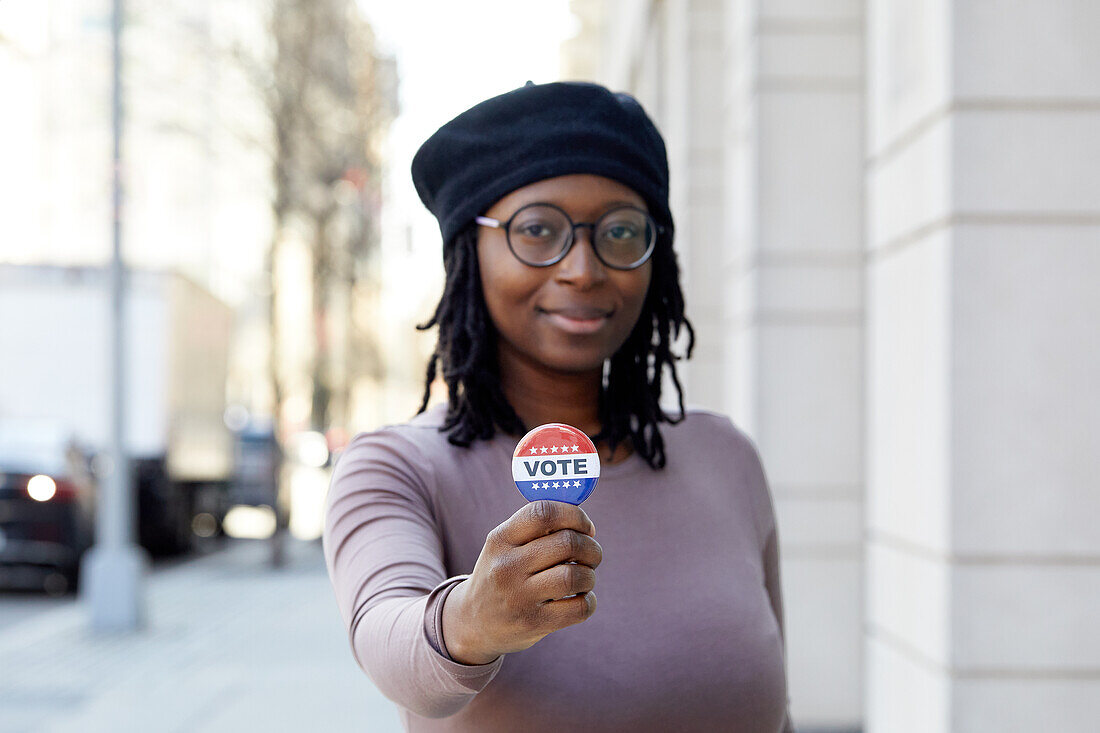 Portrait einer lächelnden Frau mit Vote-Button in der Stadt