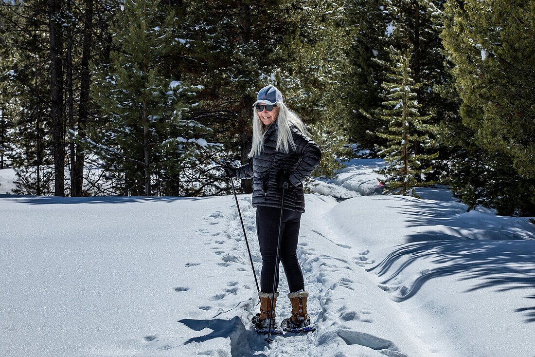 USA, Idaho, Sun Valley, Senior woman wearing snowshoes hiking in snowy forest
