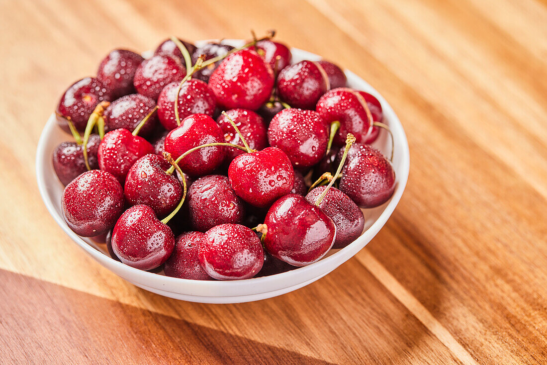 Fresh cherries in bowl on wooden surface