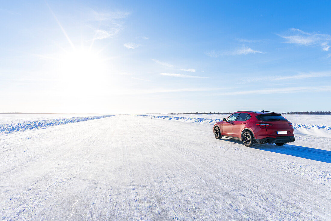Seitenansicht eines roten Autos auf einer leeren, vereisten Straße auf dem zugefrorenen See, Lulea, Norrbotten County, Lappland, Schweden, Skandinavien, Eurupe