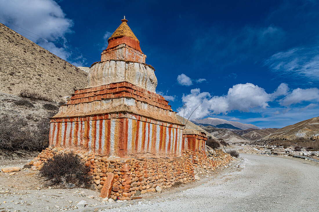 Bunt bemalter buddhistischer Stupa vor Berglandschaft, dahinter Erosionslandschaft und Häuser von Garphu, Garphu, Königreich Mustang, Himalaya, Nepal, Asien