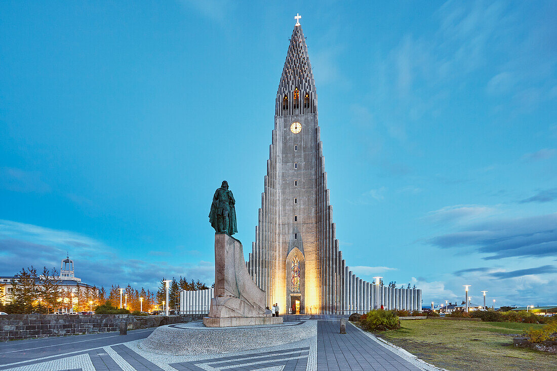 Blick in der Abenddämmerung auf die Turmspitze der Hallgrimskirkja-Kirche, vor der eine Statue von Leifur Eriksson, dem Gründer Islands, steht, im Zentrum von Reykjavik, Island, Polarregionen