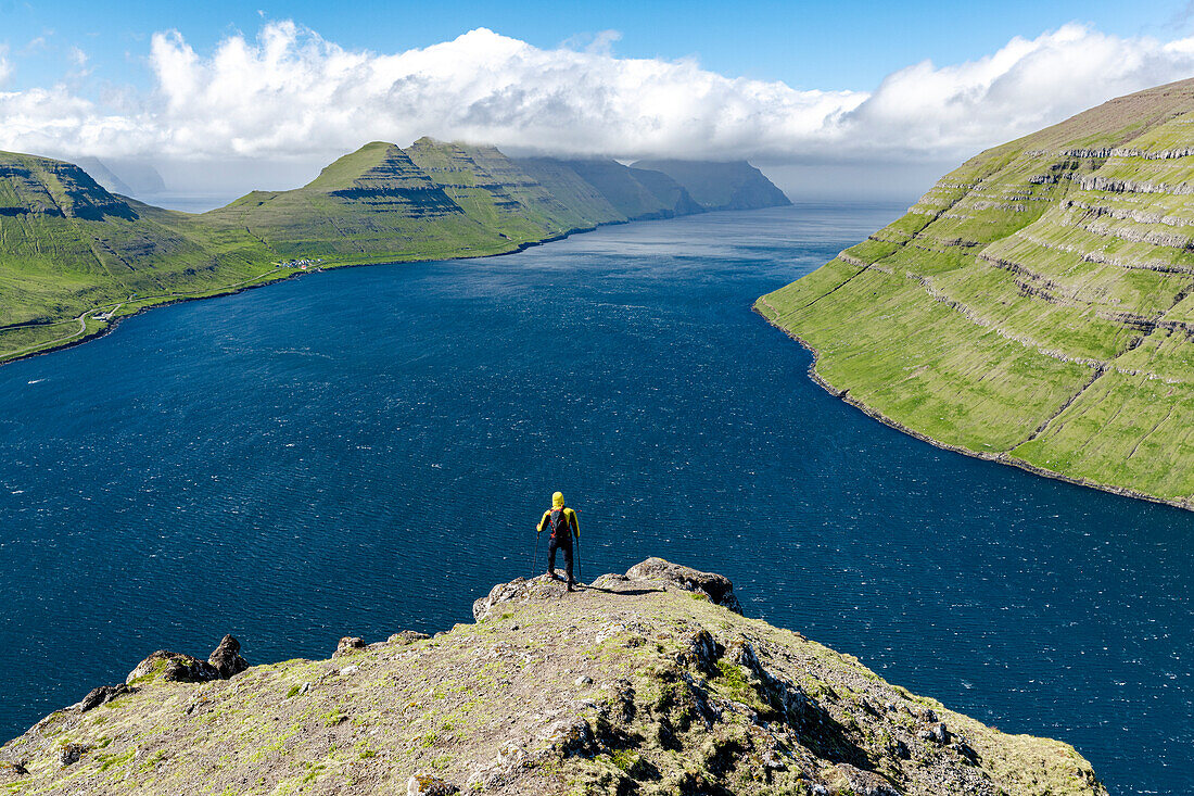 High angle view of hiker admiring mountains and ocean standing on top of a mountain, Klaksvik, Bordoy Island, Faroe Islands, Denmark, Europe
