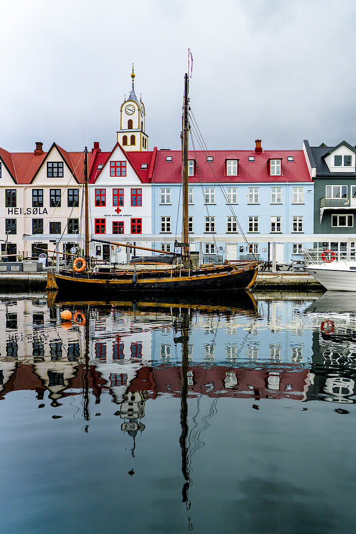Altes Holzschiff und bunte Gebäude spiegeln sich im Wasser im Hafen von Torshavn, Streymoy Island, Färöer Inseln, Dänemark, Europa