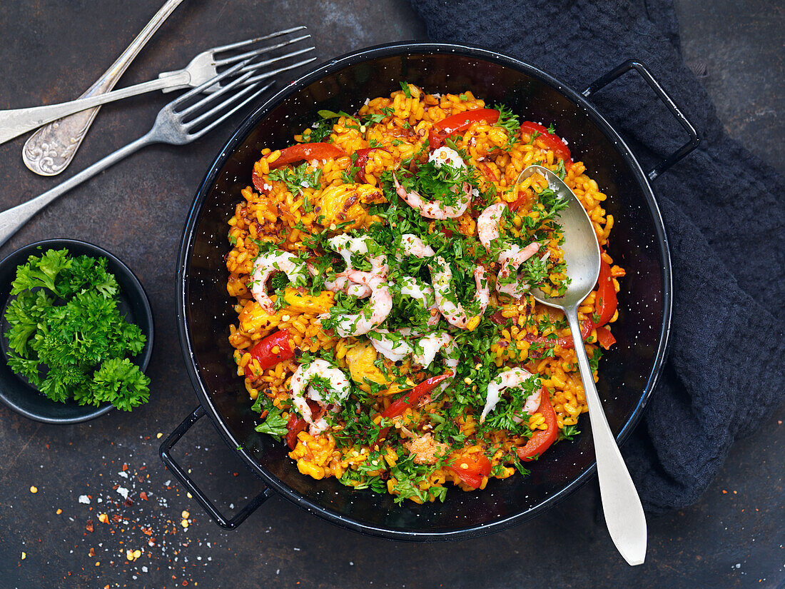 Paella mit Garnelen, roter Paprika und Petersilie