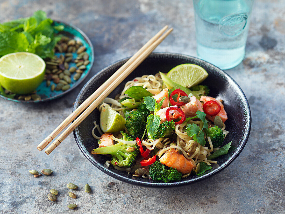 Wok-Nudeln mit Lachs, Brokkoli, Limette, Kürbiskernen, Kräutern und Chili