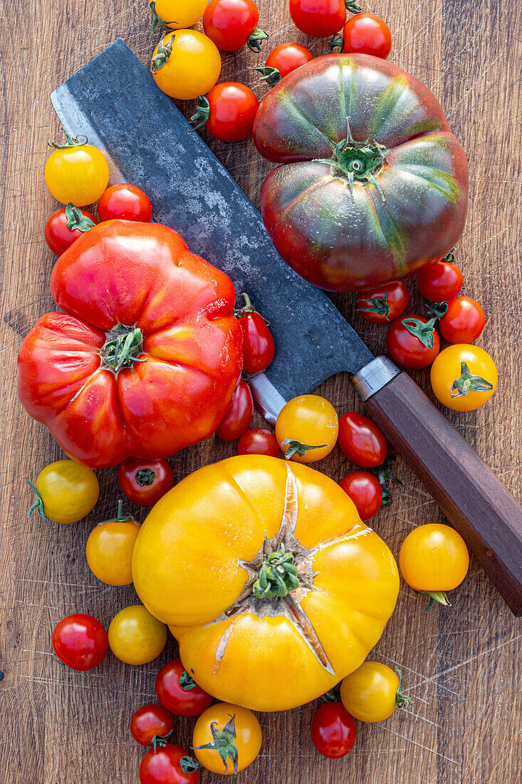 Verschiedene Tomatensorten und Küchenbeil auf Holzbrett