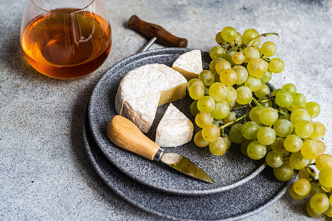 Brie und grüne Trauben auf Steinplatte und ein Glas Weißwein